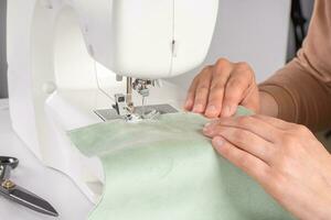 Tailor hands stitching green fabric on modern sewing machine at workplace in atelier photo
