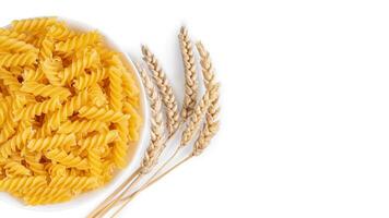 Raw pasta fusilli in bowl and wheat spikelets isolated on white background photo