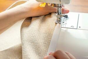 Female hands stitching white fabric on modern sewing machine. Close up view of sewing process. photo