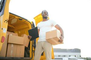 Low Angle View Of Loader Man Standing Near The Van Holding Cardboard Box photo