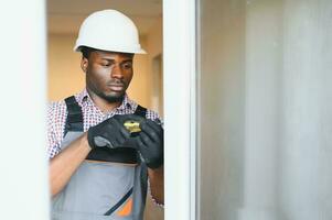 Young African Repairman In Overalls Installing Window photo