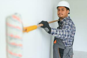 An Indian apartment repair worker paints a white wall with a roller. photo