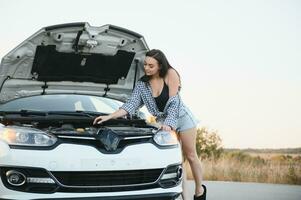 Attractive slim young girl in summer shorts and shirt repairs a broken car. A beautiful woman stands near raised car hood. photo
