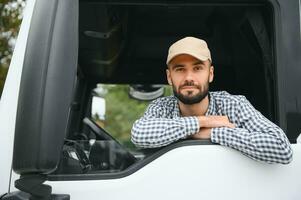 A driver sitting inside the semi-truck while looking through the open window with multiple trucks parked in the background photo