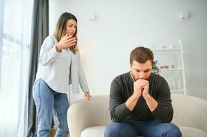 Family quarrel, man and woman sitting on sofa at home. angry woman yells at her husband photo