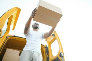 Low Angle View Of Loader Man Standing Near The Van Holding Cardboard Box photo