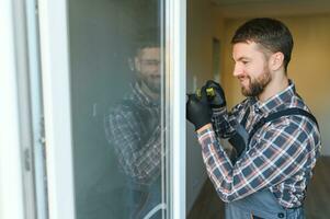 Workman in overalls installing or adjusting plastic windows in the living room at home photo