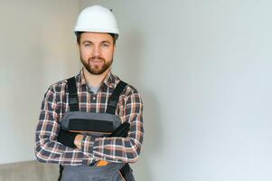 retrato de positivo, hermoso joven masculino constructor mientras trabajando a construcción sitio. foto