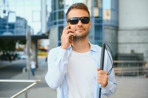 Young blind man with smartphone in city, calling photo