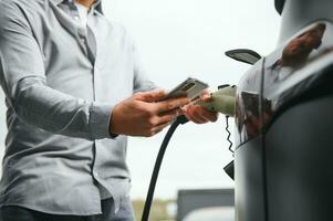 hombre participación poder cargando cable para eléctrico coche en al aire libre coche parque foto