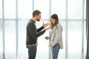 emocional hombre gesticulando y gritos a su esposa, joven Pareja teniendo pelea a hogar. Doméstico abuso concepto foto