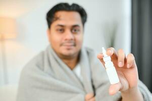 rhinitis, medicine and healthcare concept - sick indian man in blanket using nasal spray at home photo