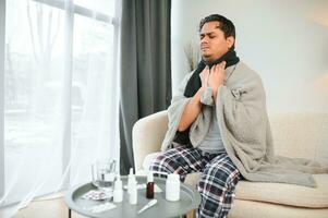 health, cold and people concept - sick young indian man in blanket having headache or fever at home photo