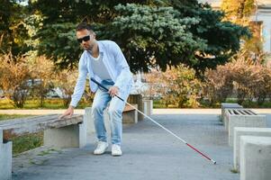 Young handsome blinded man walking with stick in town photo