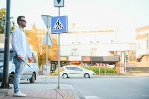 Young handsome blinded man walking with stick in town photo