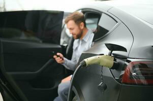 Man charging electric car by the house photo