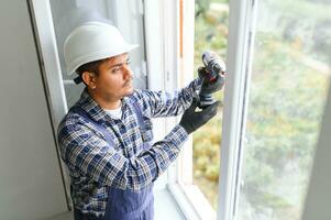 Indian Workman in overalls installing or adjusting plastic windows in the living room at home photo