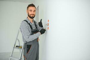 Electrician in uniform mounting electric sockets on the white wall indoors photo