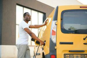 African american Man stands next to electric delivery vans at electric vehicle charging station photo