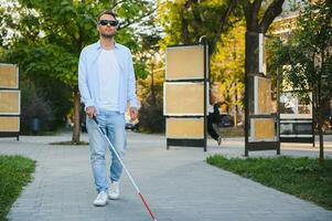 Young handsome blinded man walking with stick in town photo