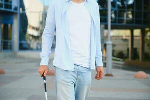 Young handsome blinded man walking with stick in town photo