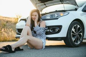 Beautiful young girl sitting at a broken car on the road desperate to get help photo