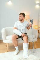 man recovery from accident fracture broken bone injury with leg splints in cast neck splints collar arm splints sling support arm in living room. Social security and health insurance concept photo