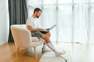 Unhealthy businessman with injured leg and arm in bandage sit on sofa at home work online on computer photo