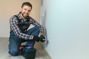 Confident professional electrician in uniform using screwdriver while replacing a socket in apartment after renovation work. photo