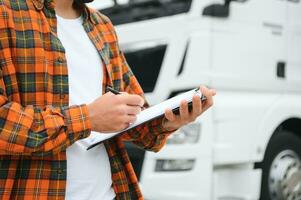 Male driver with clipboard near big truck outdoors photo