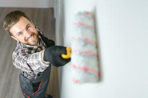 Painter painting a wall with paint roller. Builder worker painting surface with white color photo