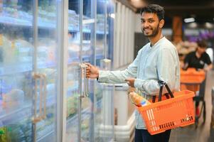 Portrait of handsome young Indian man standing at grocery shop or supermarket, Closeup. Selective Focus. photo