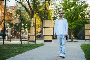 Young handsome blinded man walking with stick in town photo