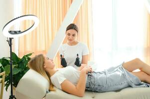 Cosmetologist applying permanent make up eyebrows for a client in a salon photo