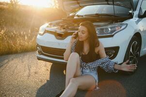 The young girl broke the car and she opened the hood and tried to repair the car on the road. A woman calls on a smartphone with a car evacuation service photo