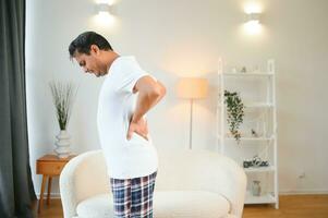 Portrait of Indian guy backache, holding spine with hand photo