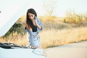 hermosa Delgado niña en camisa y pantalones cortos mira en abierto coche capucha en un la carretera foto