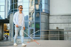 Young handsome blinded man walking with stick in town photo