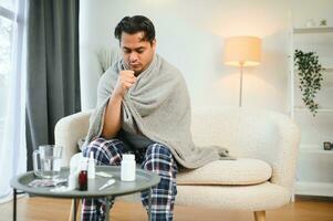 health, cold and people concept - sick young indian man in blanket having headache or fever at home photo