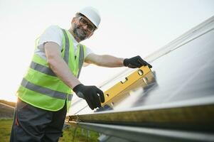 Side view of male worker installing solar modules and support structures of photovoltaic solar array. photo