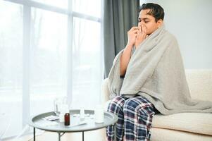 rhinitis, medicine and healthcare concept - sick indian man in blanket using nasal spray at home photo