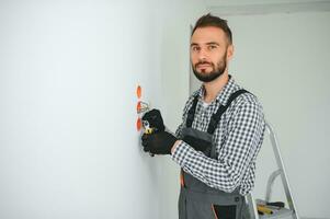 Electrician Builder at work, installation of sockets and switches. Professional in overalls with an electrician's tool. Against the background of the repair site photo