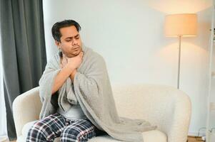 Sick young indian man suffering throat ache while sitting on bed at home photo