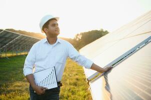 Portrait young indian technician or manager wearing formal cloths standing with solar panel. renewable energy, man standing crossed arm, copy space photo