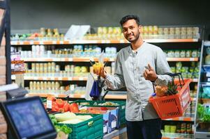 Closeup portrait, handsome young man picking up bell peppers, choosing yellow and orange vegetables in grocery store photo