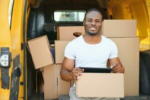 Portrait of a young African American package delivery man near a car with boxes. photo