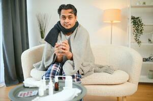 health, cold and people concept - sick young indian man in blanket having headache or fever at home photo