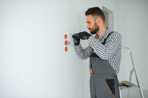 Electrician Builder at work, installation of sockets and switches. Professional in overalls with an electrician's tool. Against the background of the repair site photo