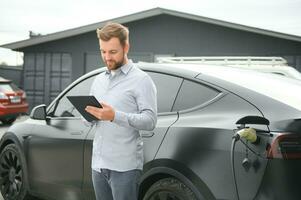 hombre cargando eléctrico coche por el casa foto