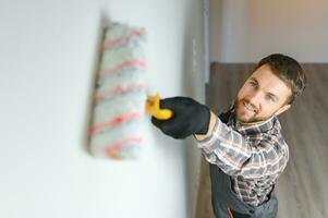 Painter painting a wall with paint roller. Builder worker painting surface with white color photo